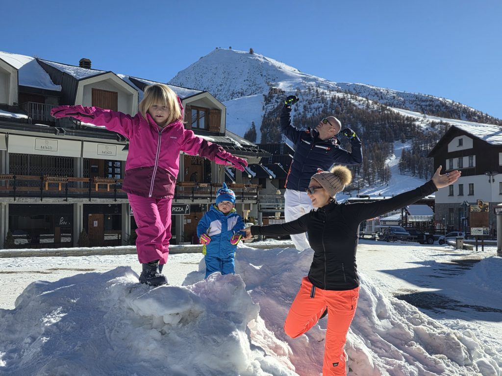 Famiglia con bambini che gioca sulla neve in montagna davanti a uno chalet, vacanza invernale sulla neve con bambini, attività all’aperto in famiglia.