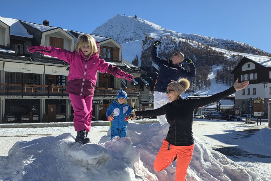 Famiglia con bambini che gioca sulla neve in montagna davanti a uno chalet, vacanza invernale sulla neve con bambini, attività all’aperto in famiglia.