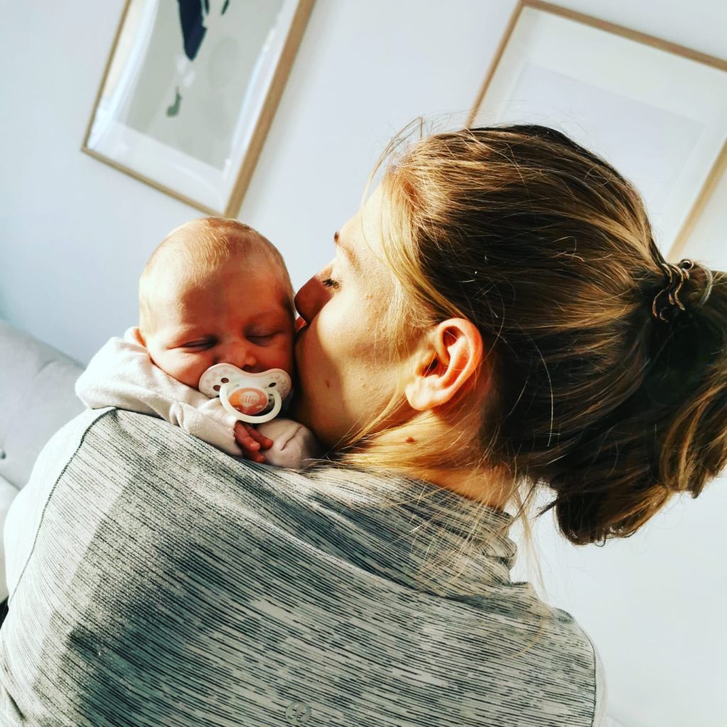 mamma di spalle che tiene in braccio il suo bambino neonato mentre gli da un bacio