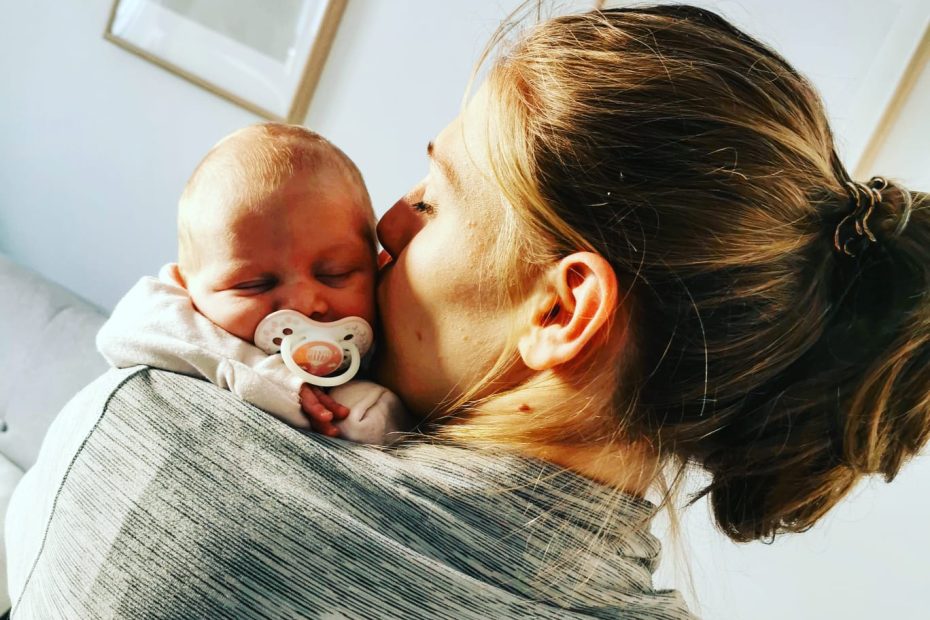 mamma di spalle che tiene in braccio il suo bambino neonato mentre gli da un bacio